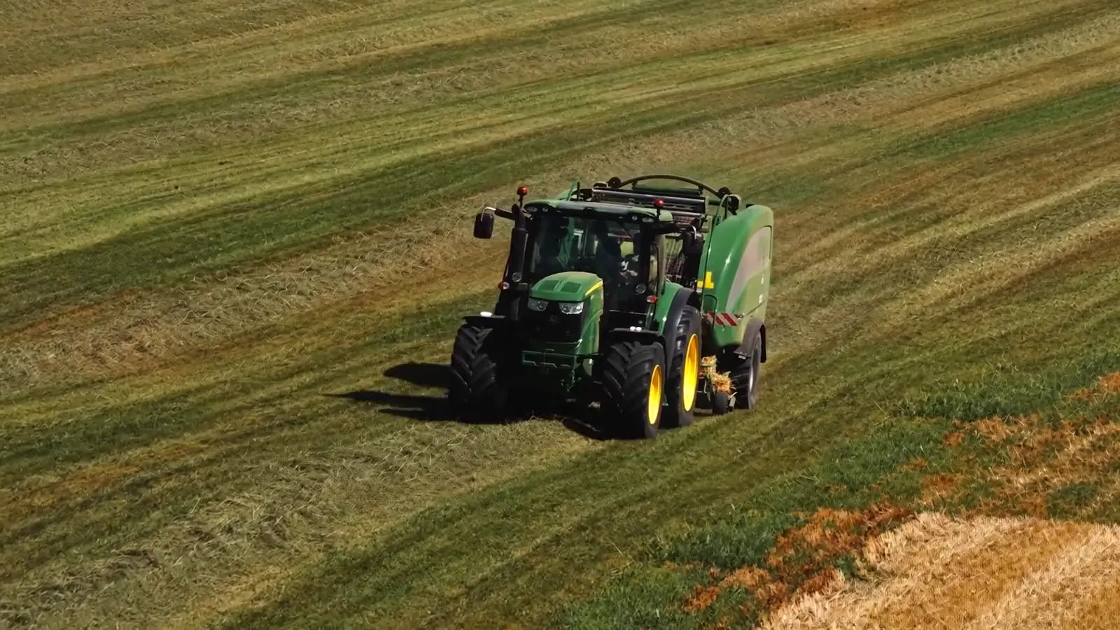 Luftaufnahme: John Deere mit McHale Rundballenpresse auf einer gemähten Wiese